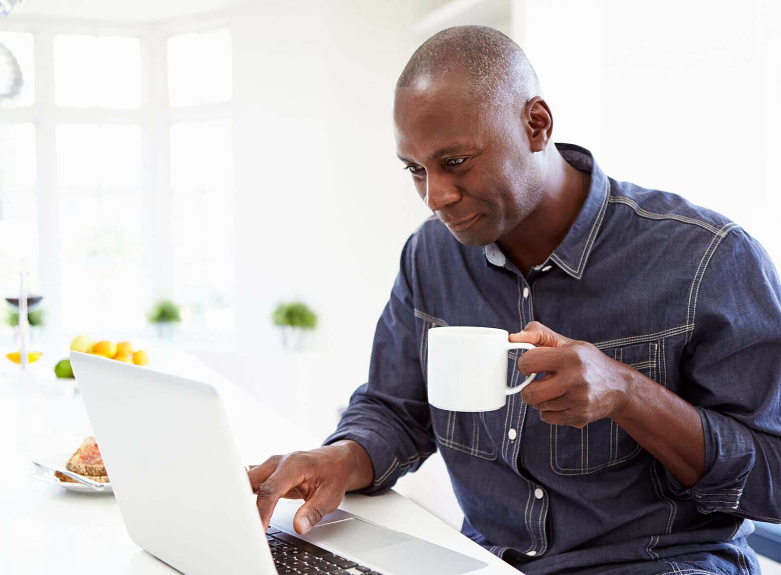 Man drinking coffee using a laptop.