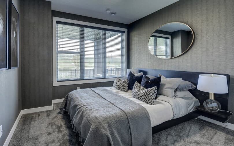 Bedroom with grey wallpaper in the Columbia plan at Cranstons Riverstone in Calgary, AB
