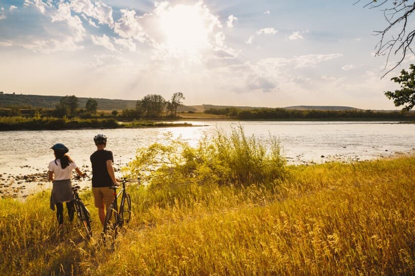 Couple riding bikes by water near Cranstons Riverstone in Calgary, AB