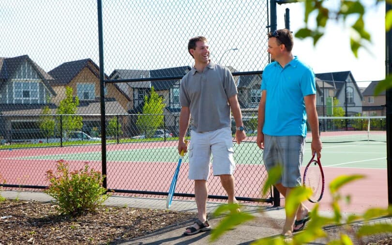 Two men walking off the tennis court with rackets in hand at Cranstons Riverstone in Calgary, AB