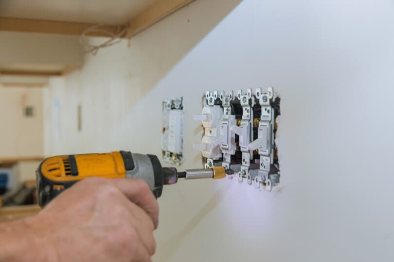 Hand holding a drill installing a light switch