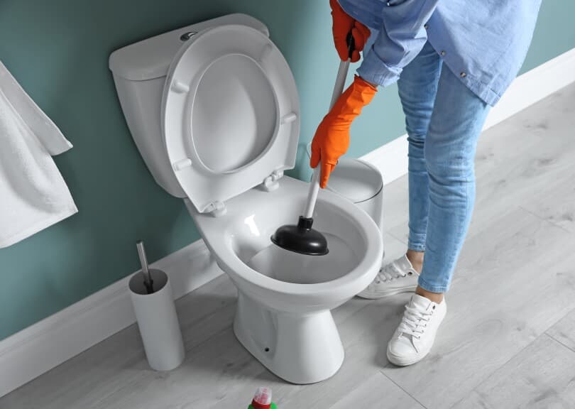 Woman using a plunger in a teal bathroom