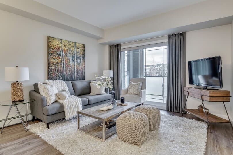Fuzzy rug, knitted poufs, and a gray couch in the great room in the Condos at Regatta in Auburn Bay, AB