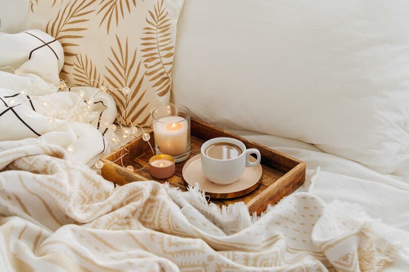 Wooden tray of coffee and candles on bed