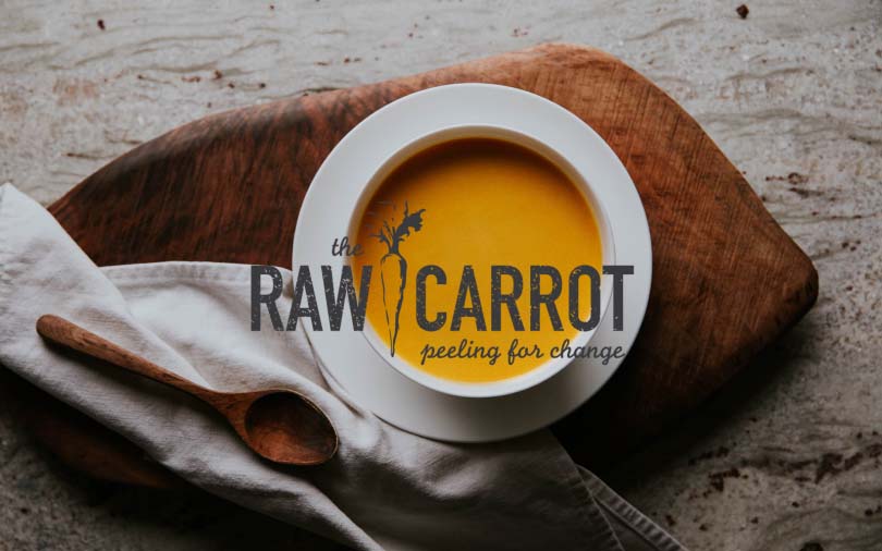 Bowl of soup with a wooden spoon with The Raw Carrot logo overlayed