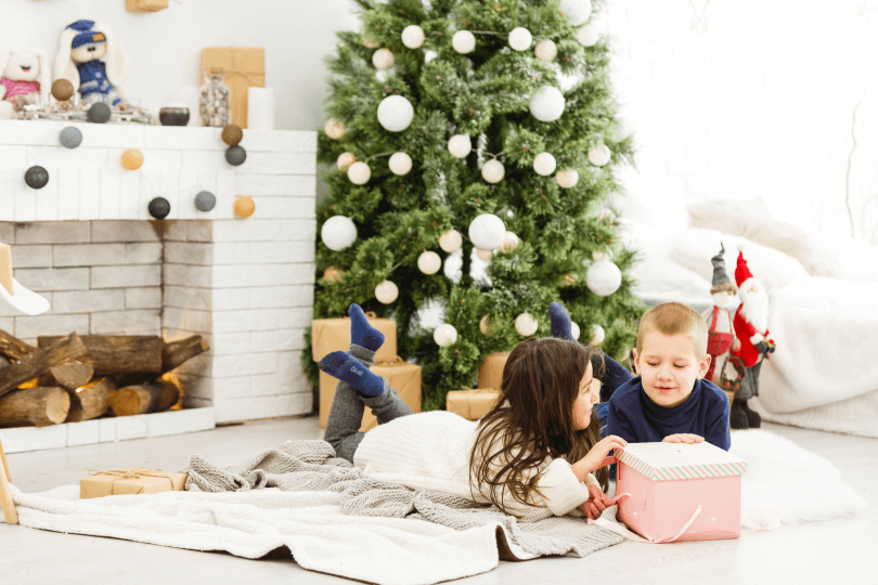 Children with a gift lying in front of a Christmas tree and fireplace