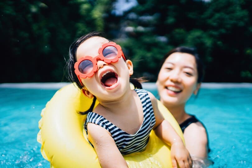 Little girl in a yellow floaty donut with her mom in a pool