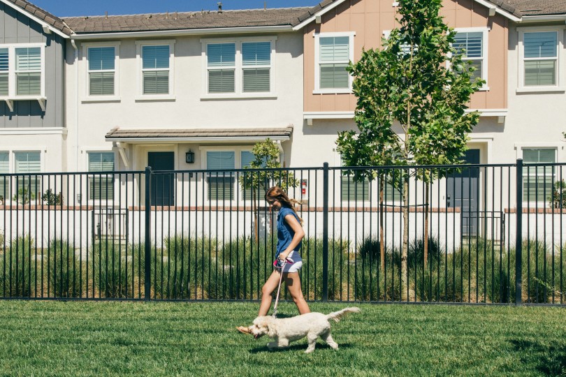 Woman walking her puppy on the grassy lawn in front of townhomes in New Haven in Ontario Ranch, CA